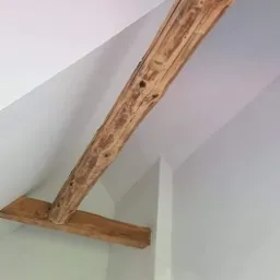 Wnętrze poddasza z widocznymi drewnianymi belkami stropowymi po malowaniu ścian na biało.