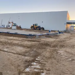 Budowa hali magazynowej w Górze w trakcie prac ziemnych, widoczny ciężki sprzęt, przygotowane fundamenty i materiały budowlane.