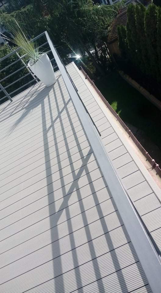 Jasnoszara deska tarasowa z kompozytu w Barcinie, z widocznymi cieniami balustrady, donica z rośliną w tle.