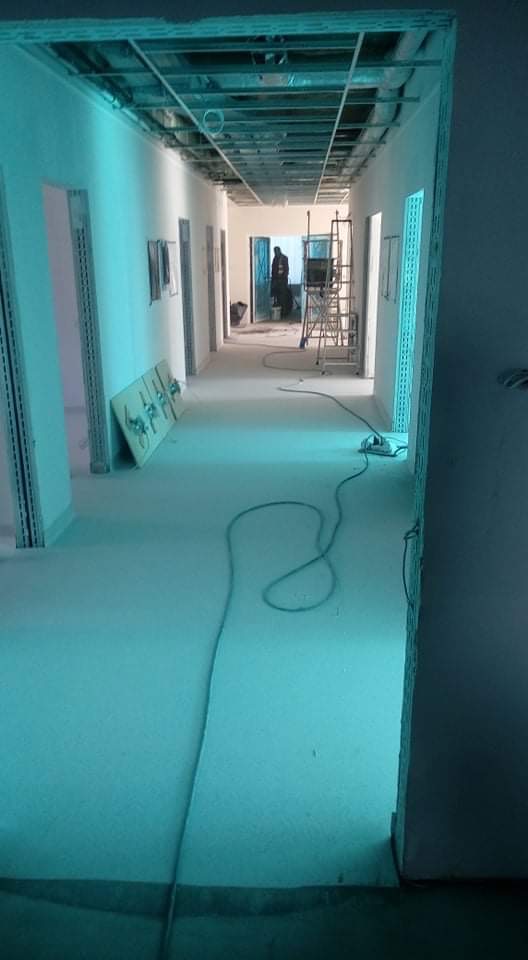 Korytarz w trakcie prac wykończeniowych: widoczne profile sufitowe, szpachlowane ściany, przewody elektryczne na podłodze, drabina w głębi.