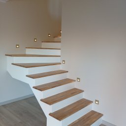 Horyzont Sebastian Zapora - Nowoczesne schody drewniane z białymi podstopnicami i subtelnym oświetleniem punktowym w ścianie. Minimalistyczny design, jasne wnętrze.