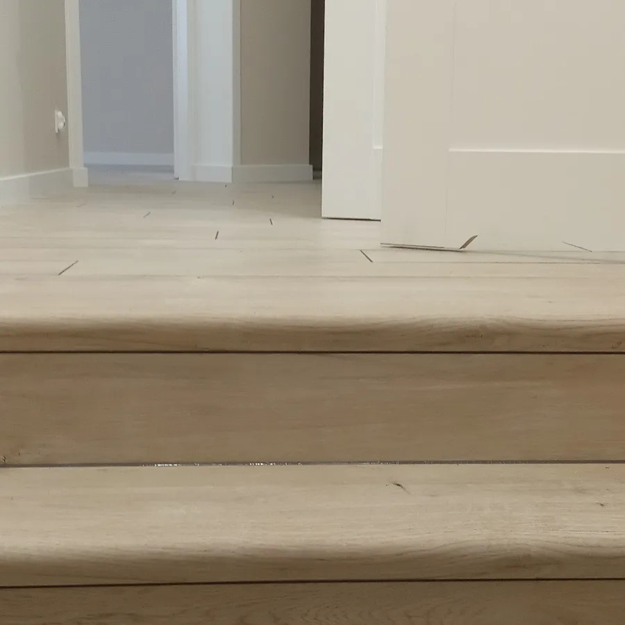 Schody wykończone jasnym drewnem, widok z dołu, minimalistyczne wnętrze z białymi drzwiami w tle.