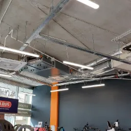 Sufit w sklepie z widocznymi elementami instalacji wentylacyjnej i klimatyzacyjnej, w tym kanały wentylacyjne w izolacji, klimakonwektor kasetonowy i metalowe korytka kablowe.