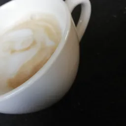 Biała filiżanka z resztką kawy latte na czarnym tle, widok z góry pod kątem.