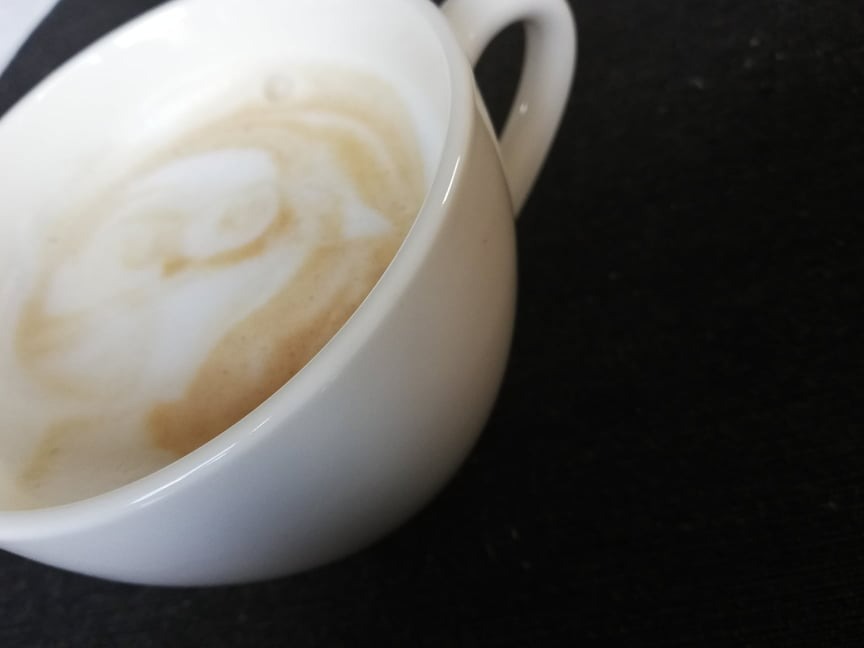 Biała filiżanka z resztką kawy latte na czarnym tle, widok z góry pod kątem.