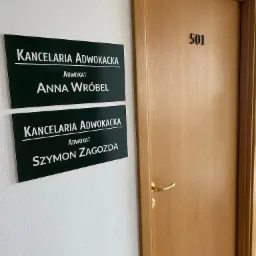 Tabliczki informacyjne 'Kancelaria Adwokacka' z nazwiskami adwokatów Anny Wróbel i Szymona Zagody obok drewnianych drzwi z numerem 501.