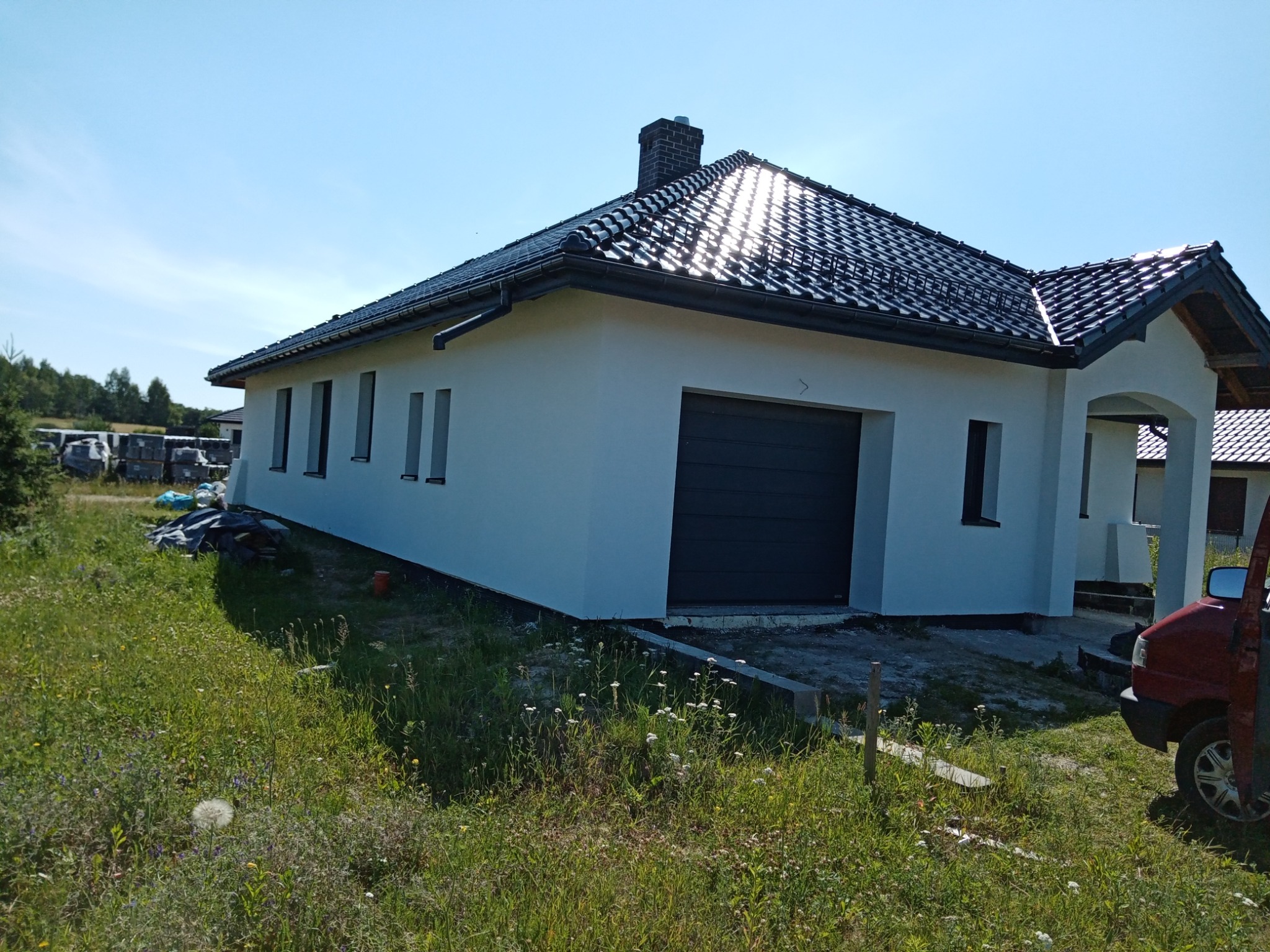 Jednorodzinny dom z szarą bramą garażową i świeżo pomalowaną białą elewacją, widok z zewnątrz w słoneczny dzień.