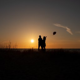 WAM Studio Fotografia - Sylwetki pary z czerwonym balonem w kształcie serca na tle zachodzącego słońca nad morzem w Polanowie.
