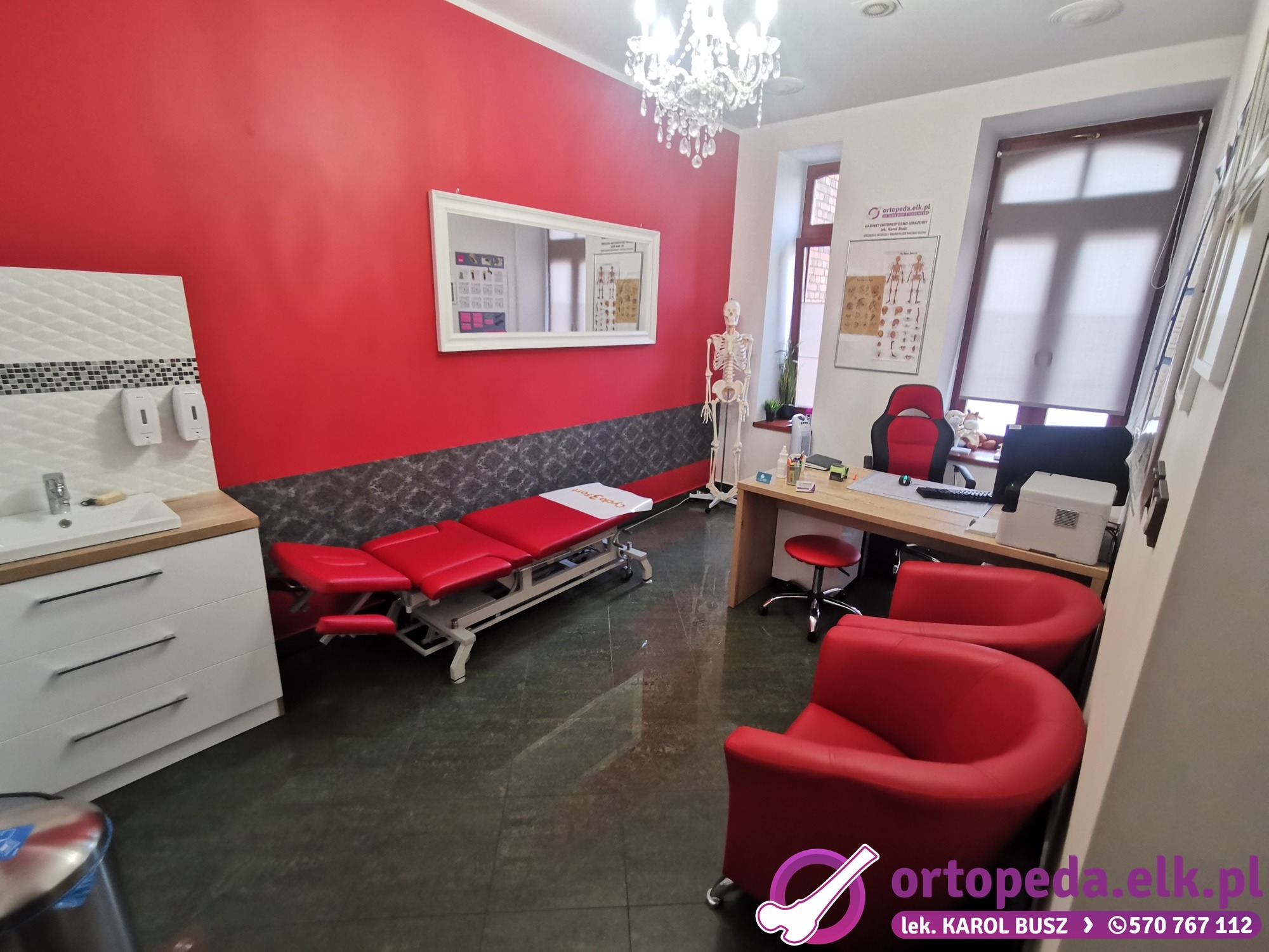 Nowoczesny gabinet ortopedyczny w Ełku. Czerwone ściany, białe meble, leżanka, krzesła i szkielet anatomiczny. Jasne oświetlenie i elegancki wystrój.
