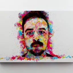 Portret mężczyzny z brodą, namalowany w stylu pop-art, z użyciem jaskrawych, rozpryskujących się farb na białym płótnie, zawieszonym na białej ścianie.