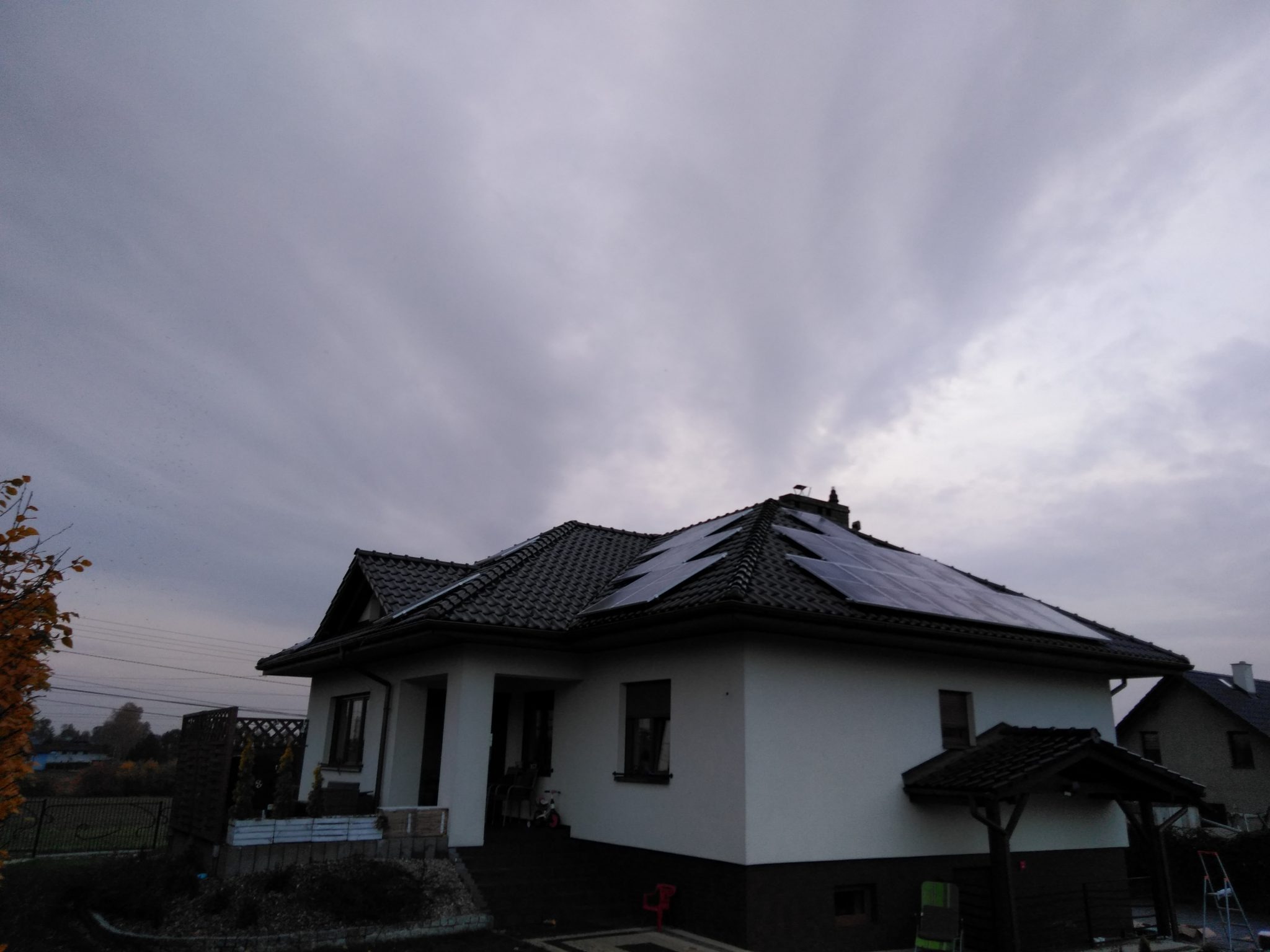 Dom jednorodzinny z panelami słonecznymi na dachu, pochmurne niebo w tle.