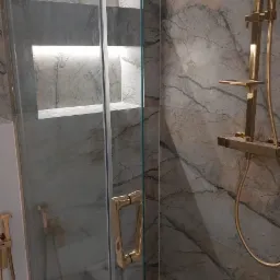 Wykończona łazienka w Tąpkowicach z kabiną prysznicową ze złotymi elementami i marmurowymi płytkami oraz wnękami z podświetleniem LED.