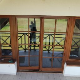 Jarosław Buczek ACTUAL COMFORT - Dwa białe klimatyzatory GREE zamontowane jeden nad drugim na ścianie pod skosem, obok brązowych okien balkonowych z widokiem na zielony trawnik.