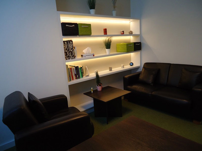 Gabinet z czarną skórzaną sofą i fotelem, regał z podświetleniem LED, dekoracje i książki.