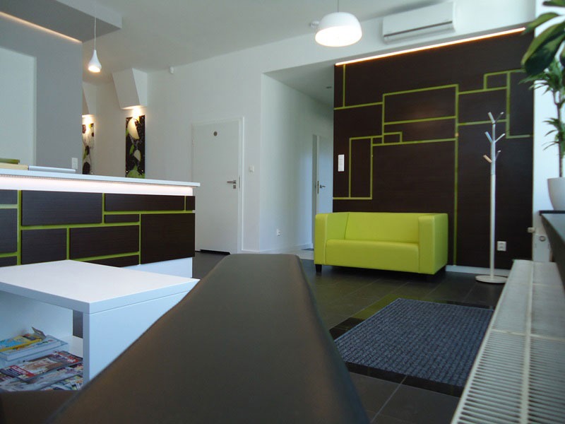 Nowoczesne wnętrze gabinetu dietetycznego z recepcją, zieloną sofą i dekoracyjną ścianą z geometrycznym wzorem.