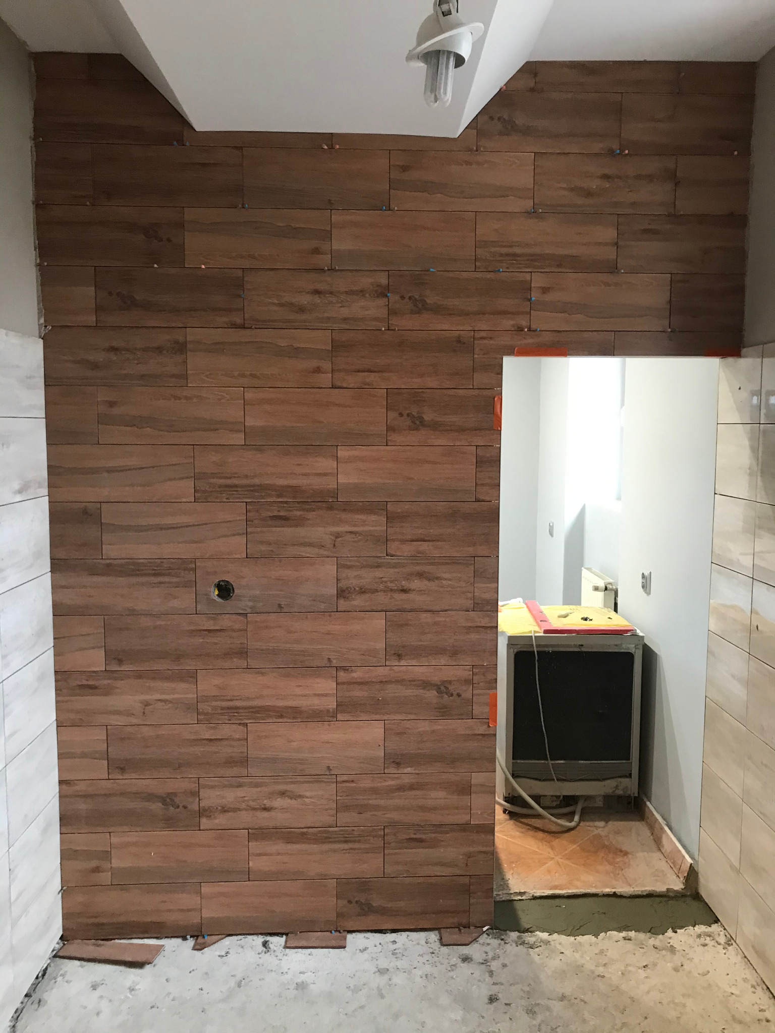 Ściana w trakcie układania płytek imitujących drewno w kuchni, widoczne krzyżyki dystansowe i otwór na gniazdko elektryczne.