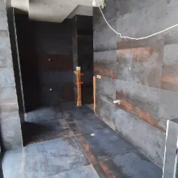 Łazienka w trakcie wykańczania z dużymi, ciemnymi płytkami imitującymi metal na ścianach i podłodze, widoczne pionowe podpory z listew drewnianych i plastikowych krzyżyków dystansowych, surowa...