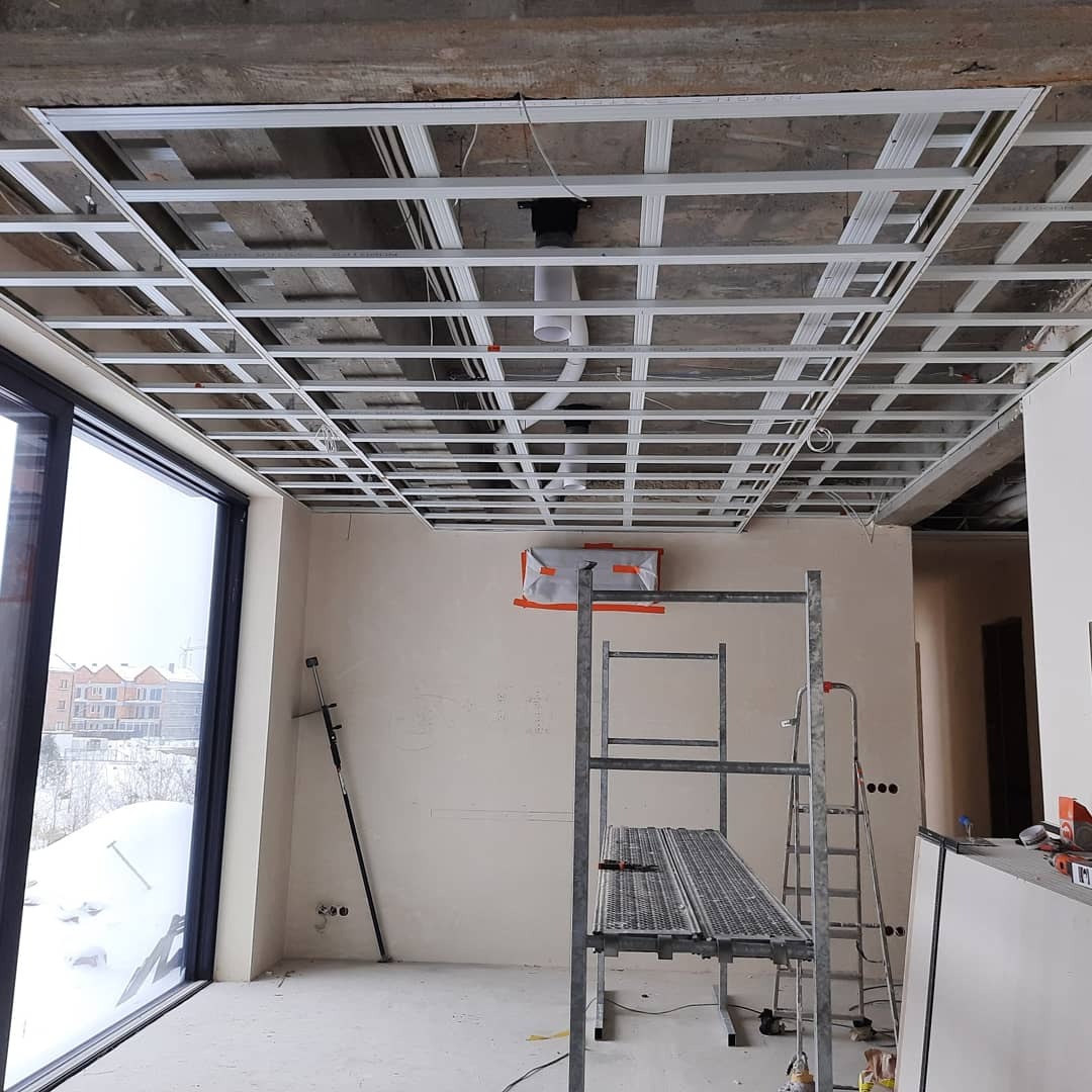 Szkielet metalowej konstrukcji sufitu podwieszanego w trakcie montażu w Sączowie, widoczne profile, rury wentylacyjne i drabina.