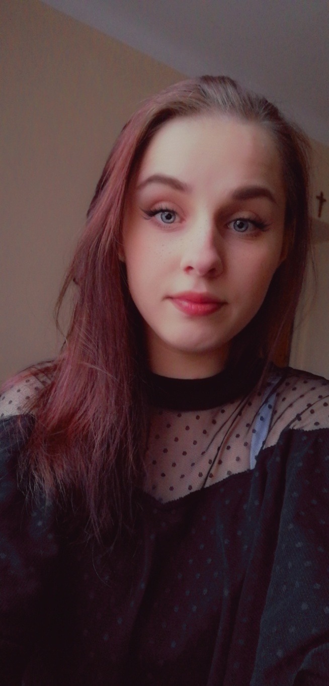 Portret młodej kobiety z różowymi włosami i niebieskimi oczami, ubrana w czarną bluzkę w kropki, delikatny makijaż i subtelny uśmiech.