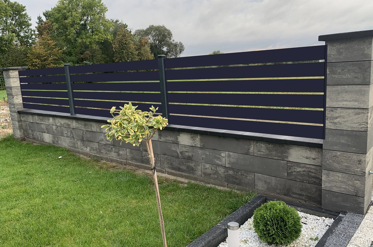 Nowoczesne ogrodzenie panelowe z poziomych desek w kolorze antracytowym, osadzone na murku z szarych, betonowych bloczków, z widocznym trawnikiem i ozdobnym drzewkiem.