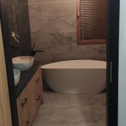 Nowoczesna łazienka z marmurowymi płytkami, wolnostojącą białą wanną, drewnianą szafką pod umywalką z dwoma umywalkami w odcieniach szarości i oknem z drewnianymi żaluzjami, widziana zza czarnej...