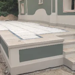 Wykończony taras z płytkami w odcieniach beżu i szarości, otoczony świeżo pomalowaną elewacją w kolorze oliwkowym z kremowymi detalami, widoczne schody i fragment ogrodu w tle.