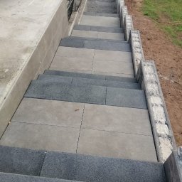 Ipo Sp. z o. o. - Schody zewnętrzne wyłożone kombinacją jasnoszarych płyt i ciemnoszarej kostki z fakturą, widok z góry na dół, z elementami rusztowania w tle.