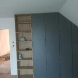 Montaż zabudowy meblowej pod skosem z otwartym regałem, widoczne przygotowania do prac wykończeniowych w tle.