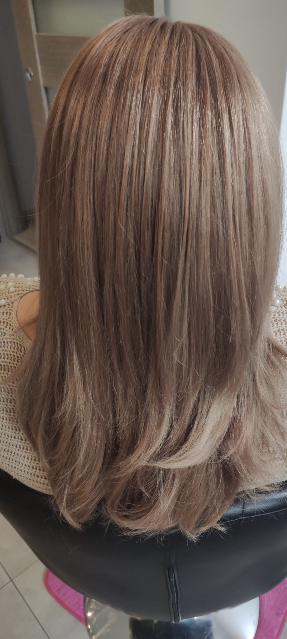 Widok z tyłu na świeżo ostrzyżone i ufarbowane włosy w odcieniach beżu i blondu, z delikatnymi falami na końcach i widoczną strukturą włosa.