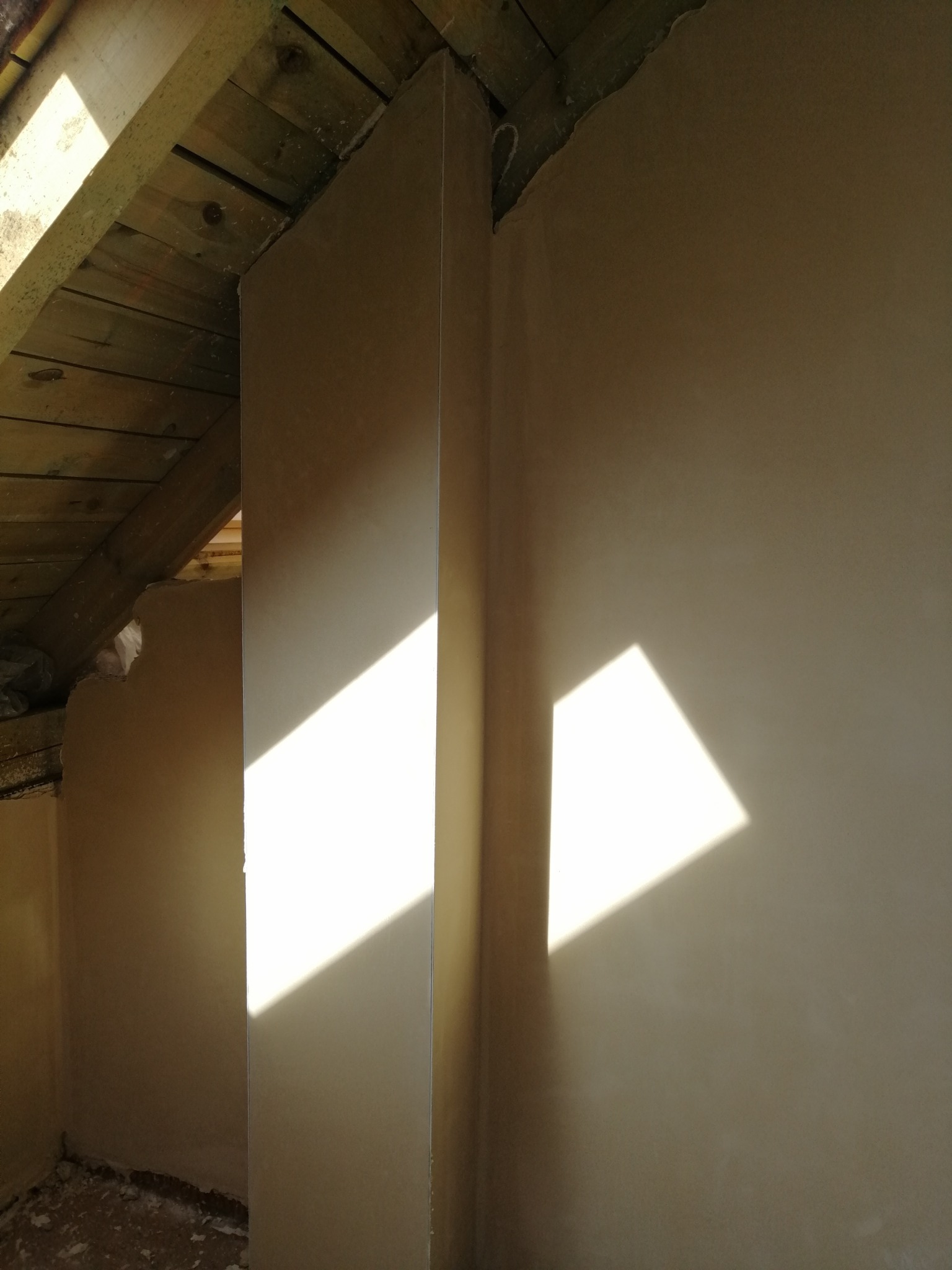 Ściana poddasza po szpachlowaniu z widocznym załamaniem dachu i padającym światłem słonecznym.