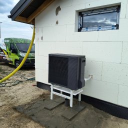 Eco Therm - Zamontowana pompa ciepła Panasonic Aquarea na elewacji budynku z izolacją styropianową. Żółty wąż obok, w tle firmowy bus EcoTherm.