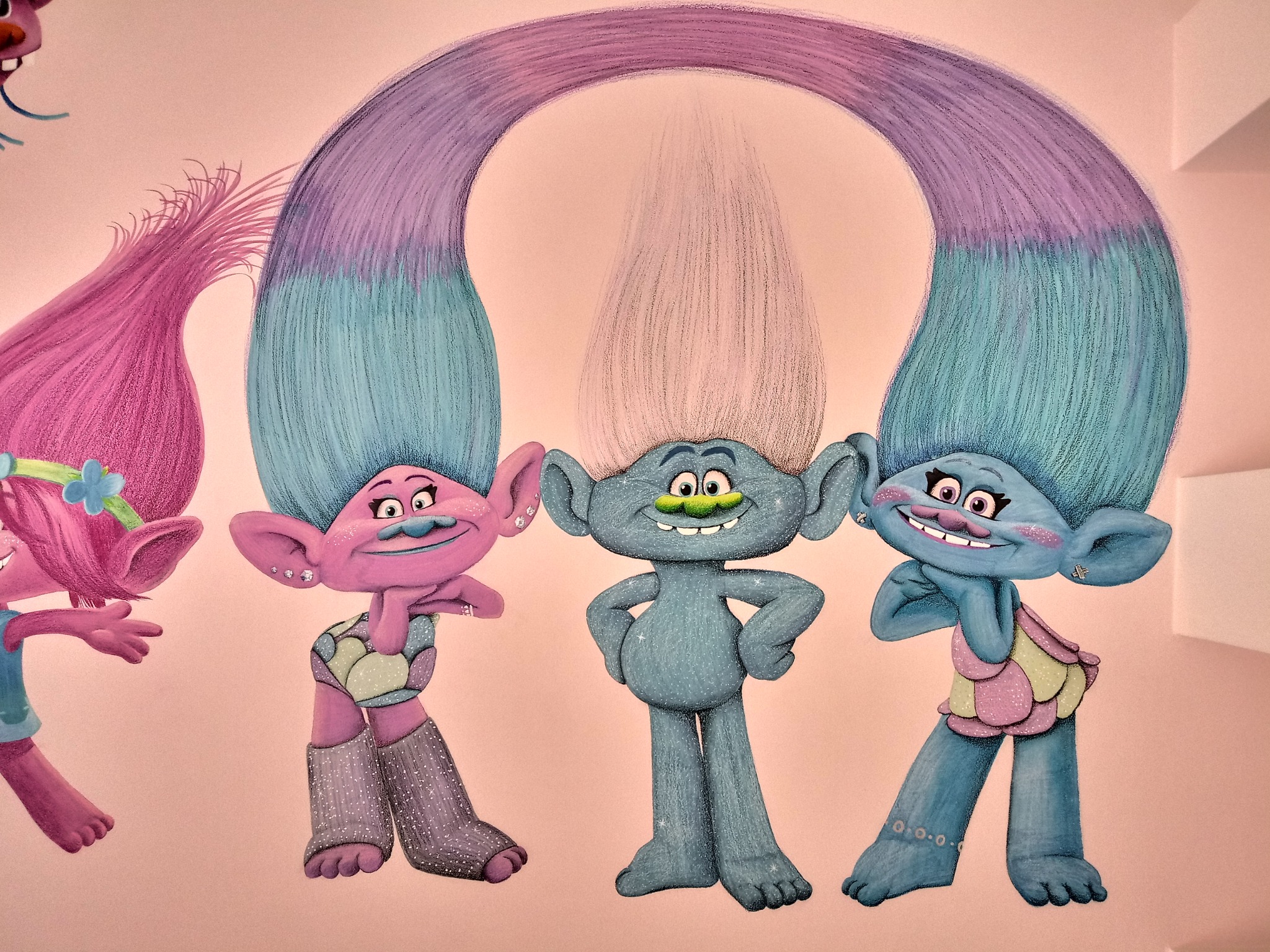 Malowidło ścienne przedstawiające postacie z bajki Trolle w pastelowych kolorach, z brokatowymi detalami na ubraniach i włosach, na jasnoróżowym tle.