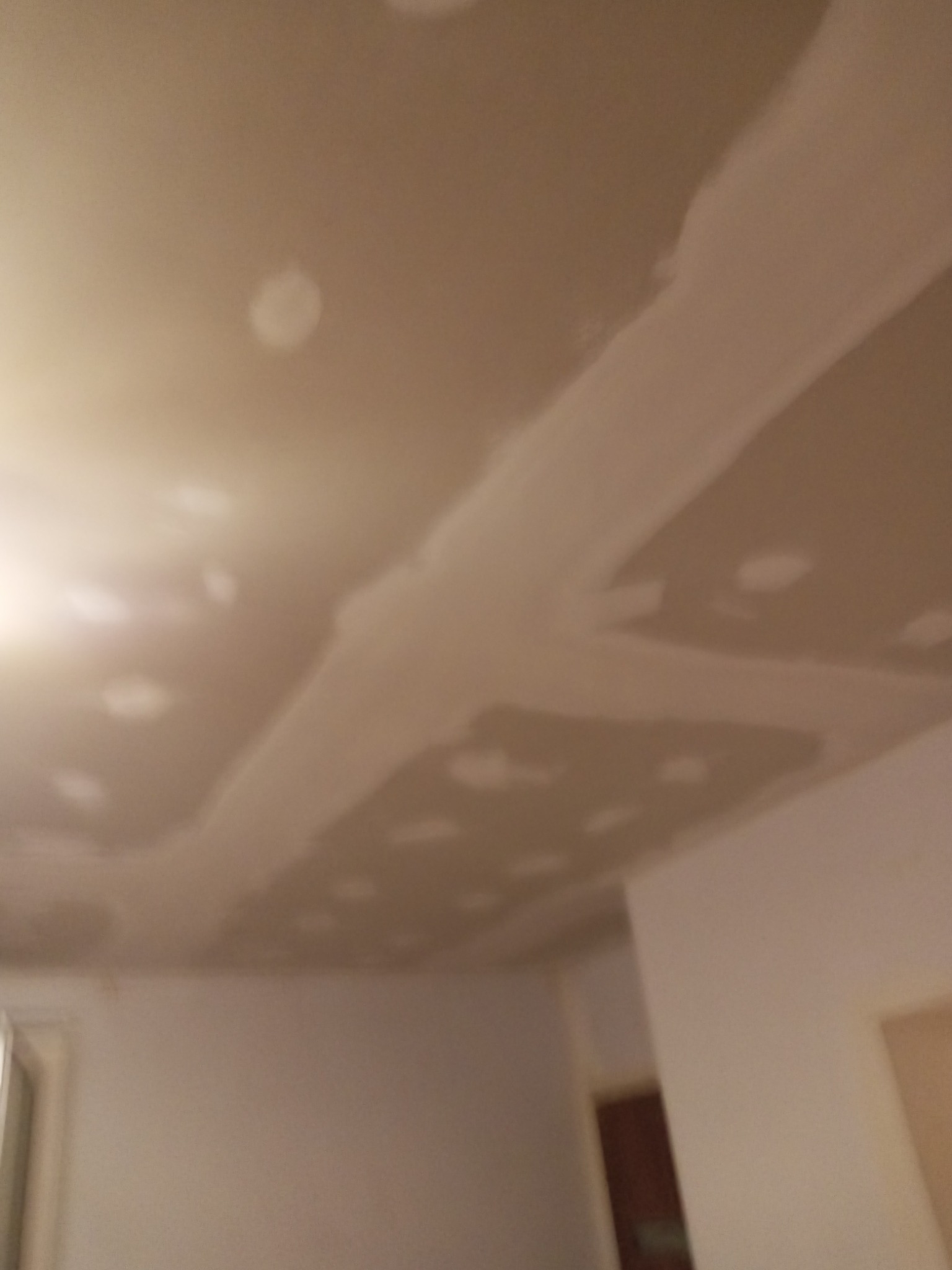 Niedokończony sufit z płyt kartonowo-gipsowych, widoczne łączenia i szpachlowane miejsca po wkrętach, przygotowany do malowania.