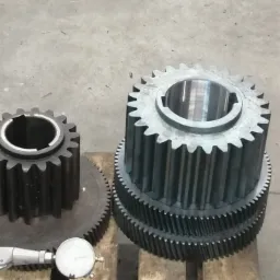 Stos metalowych kół zębatych o różnej wielkości na drewnianej palecie, obok narzędzie pomiarowe z tarczą.