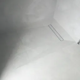 Nowoczesna kabina prysznicowa z odpływem liniowym, wyłożona jasnoszarymi, matowymi płytkami wielkoformatowymi.