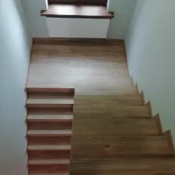 Schody wykończone panelami drewnopodobnymi, widok z góry na dół, z oknem dachowym w tle.