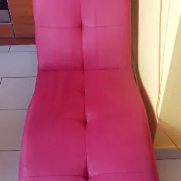 Różowa, tapicerowana leżanka z zagłówkiem, widoczna na tle kuchni z białymi płytkami podłogowymi.