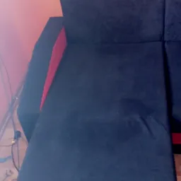 Ciemna, narożna kanapa z czerwonymi akcentami po czyszczeniu, widoczna rura odkurzacza na podłodze.