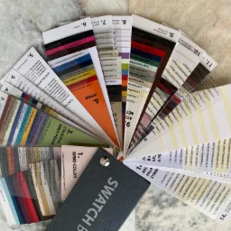 Paleta próbek kolorów i faktur papieru, ułożona wachlarzowo na marmurowym tle, z widocznym napisem 'SWATCH BOOK'.