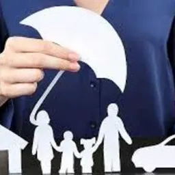 Kobieta w niebieskiej bluzce trzyma biały, papierowy parasol nad papierową rodziną, domem i samochodem, symbolizując ochronę.