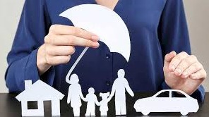 Kobieta w niebieskiej bluzce trzyma biały, papierowy parasol nad papierową rodziną, domem i samochodem, symbolizując ochronę.