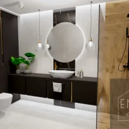 Nowoczesna łazienka z czarnymi szafkami z złotymi akcentami, umywalką nablatową o geometrycznym kształcie, okrągłym lustrem z podświetleniem LED, drewnopodobną ścianą prysznicową i wiszącą toaletą.