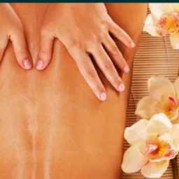 Dłonie na plecach podczas zabiegu relaksacyjnego, w tle bambusowa mata, orchidee i świece.