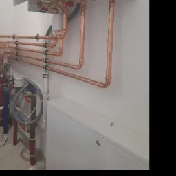 Nowoczesny piec gazowy z miedzianymi rurami instalacji grzewczej, zamontowany na białej ścianie w kotłowni.