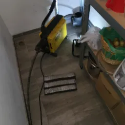 Żółta maszyna do udrażniania rur Rems z wężem na szarej podłodze. W tle metalowy regał z różnymi przedmiotami.