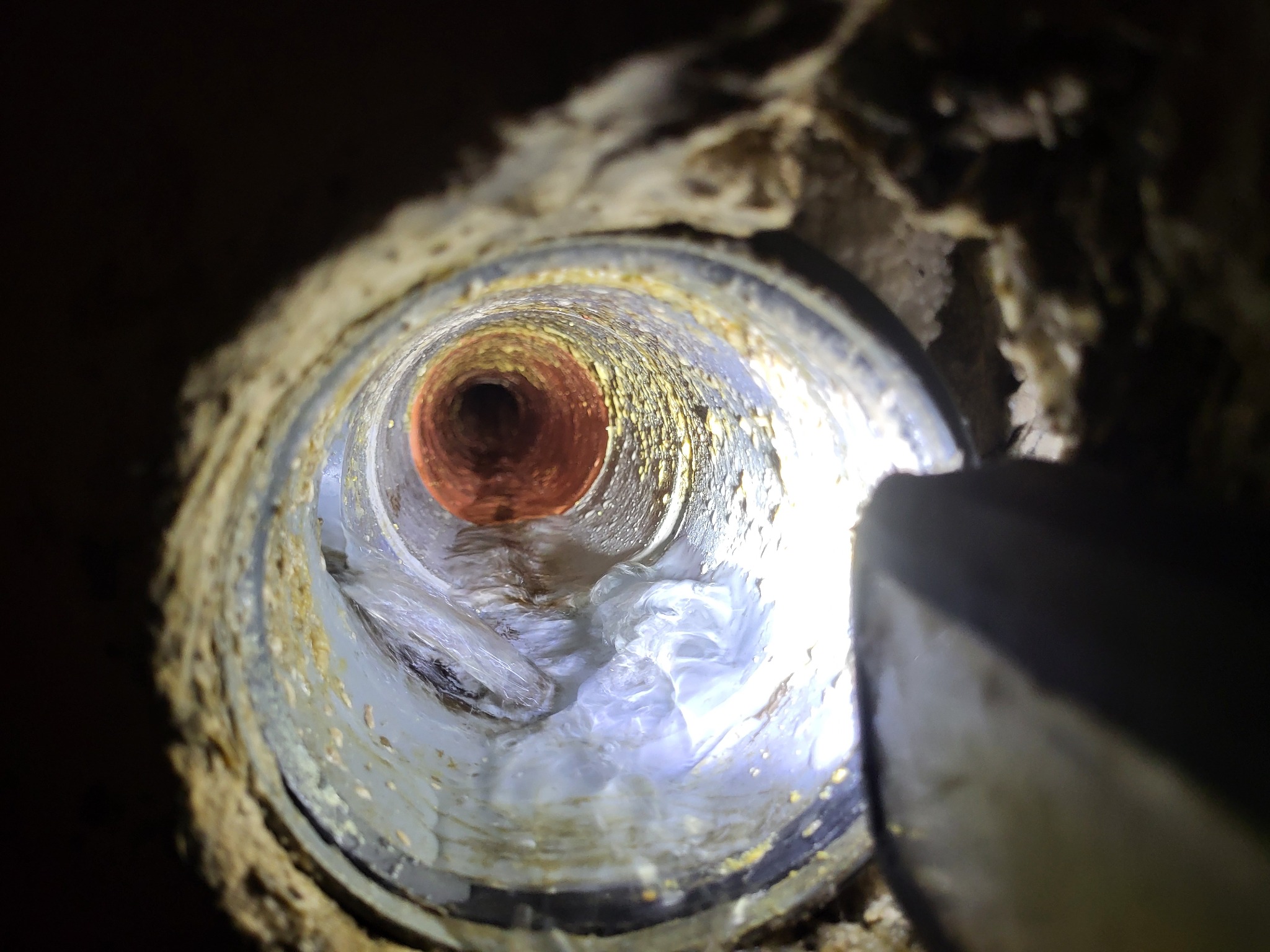 Wnętrze rury kanalizacyjnej z resztkami po czyszczeniu, widoczne osady na ściankach i częściowo przepływająca woda, oświetlone światłem.