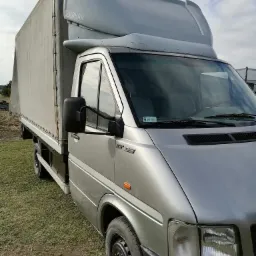 Srebrny samochód dostawczy z plandeką i zabudową kabiny sypialnej marki Markar, zaparkowany na trawiastym terenie.