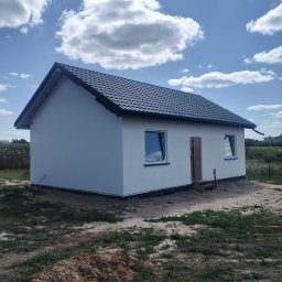 Dariusz -Termo Dom Ostrów Wlkp - Nowo wybudowany parterowy dom z białymi ścianami i ciemnym, dwuspadowym dachem z dachówki. Przed wejściem tymczasowy drewniany stopień. Niezagospodarowany teren wokół.