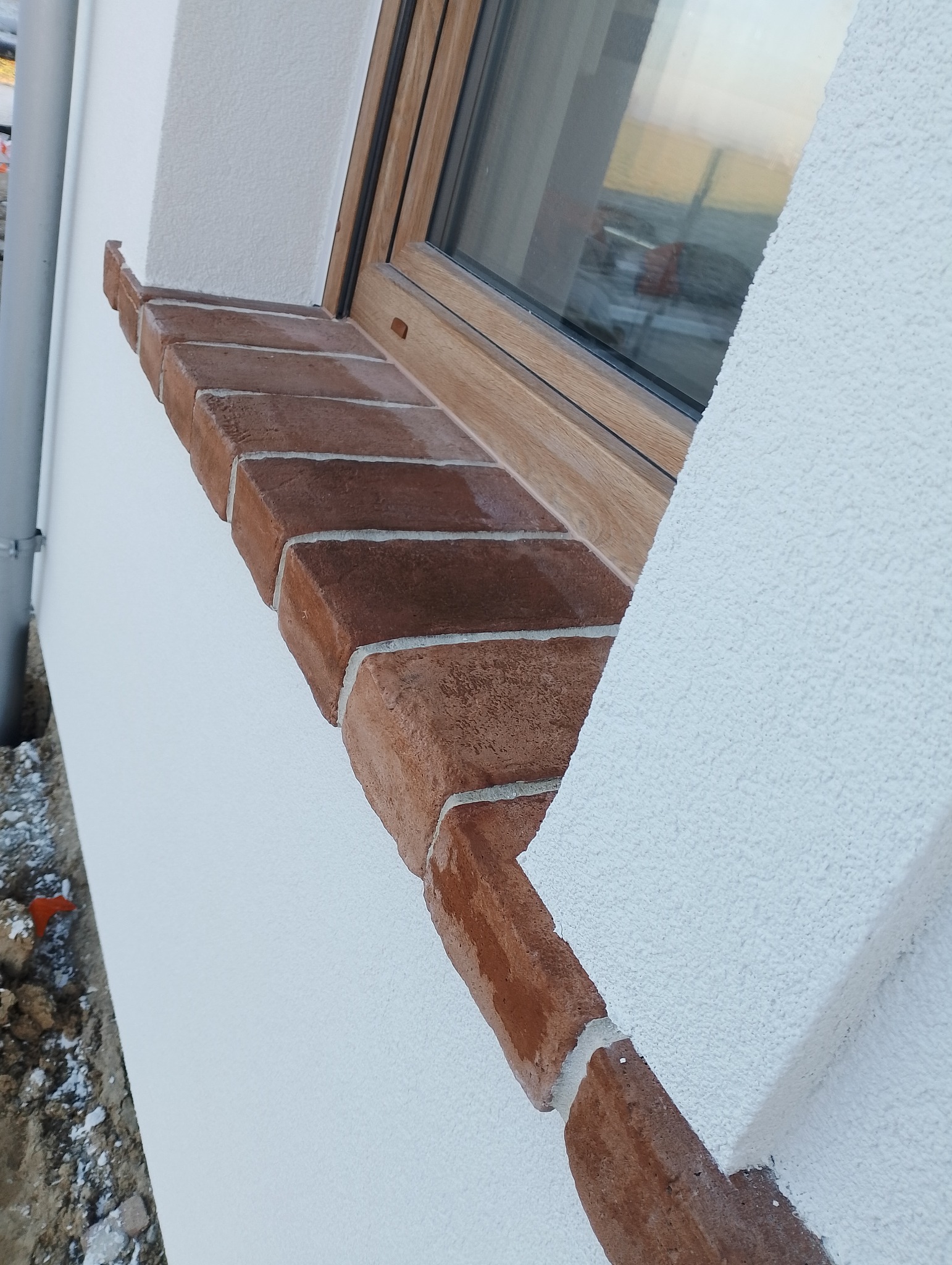 Elewacja domu z oknem i ceglanym parapetem, widoczna struktura tynku.