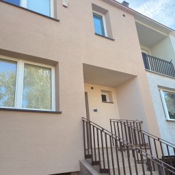 POINT PRIME SOLUTIONS Sp. o.o. - Jasnobeżowa, teksturowana elewacja budynku mieszkalnego z białymi oknami, wejściem z brązowymi balustradami i schodami wyłożonymi płytkami, widok z dołu.